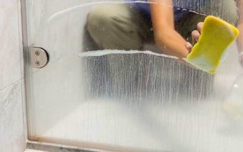 A person wipes a frosted glass shower door with a microfiber cloth, removing soap scum and water spots