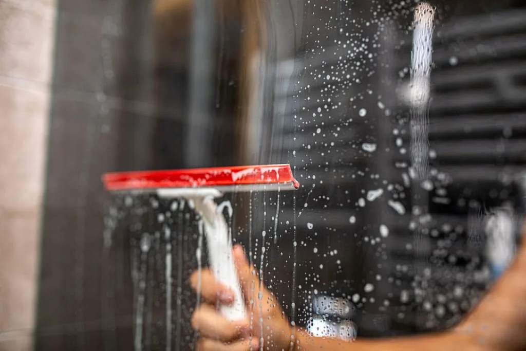 A spray bottle filled with a vinegar and water mix sits beside a frosted glass shower door, ready for cleaning