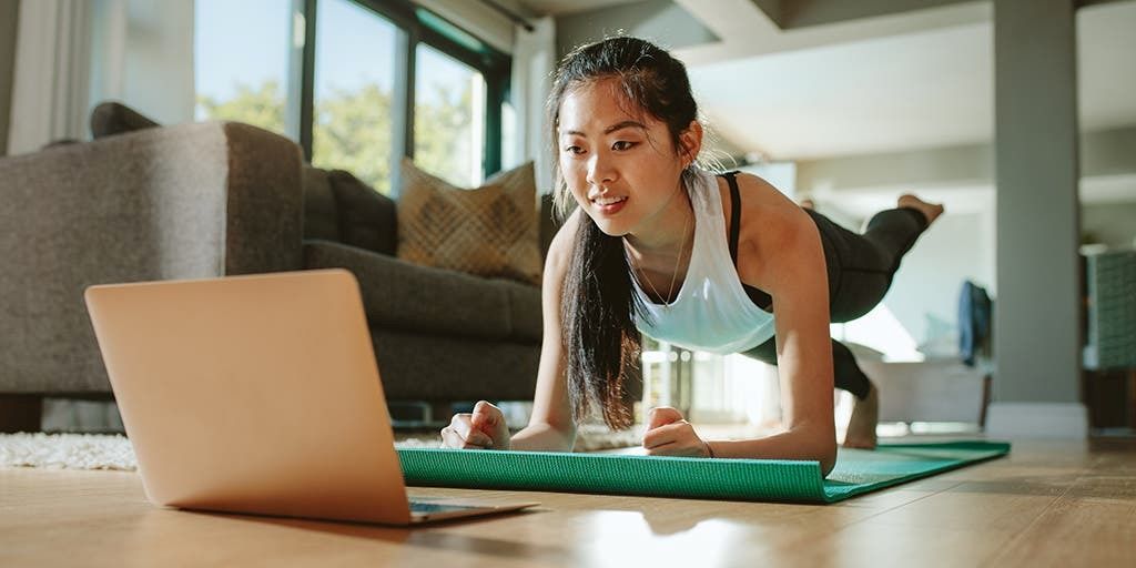 A woman follows a full-body stretch plan on a mat in her home office, highlighting fitness for busy people