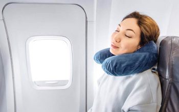 Woman sleeping peacefully on plane with twisted Dot&Dot memory foam travel pillow supporting her neck