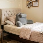A soft tufted headboard attached to a dorm twin XL bed with a back support pillow placed against it